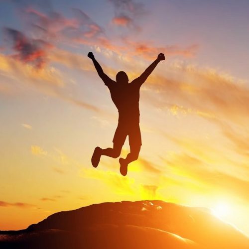 Happy man jumping for joy on the peak of the mountain, cliff at sunset. Success, winner, happiness